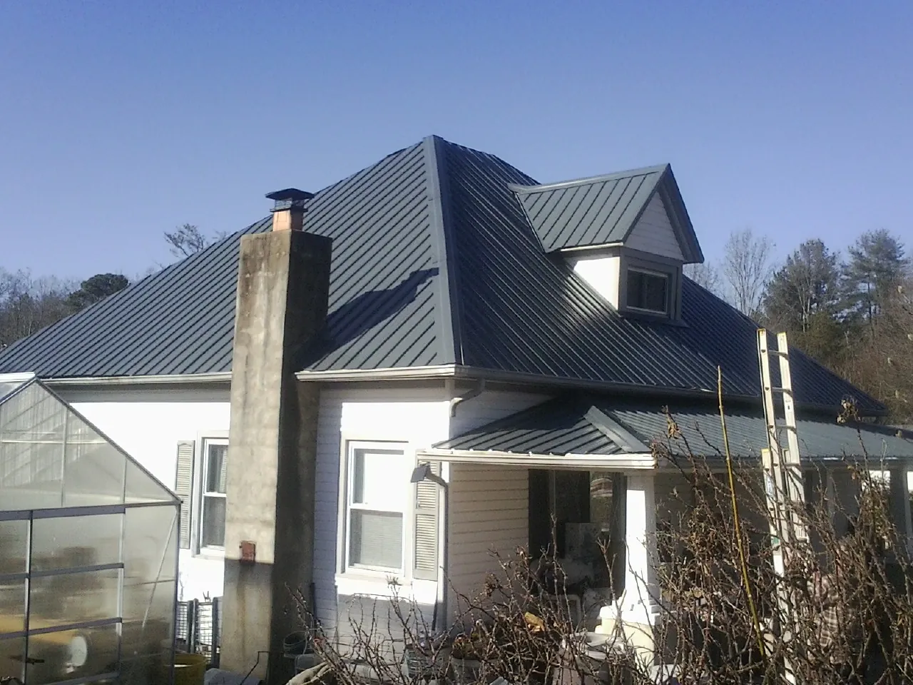 Dark blue standing seam metal roof on a white farmhouse with dormer — Slate & Tile Roof Repair by Roofing Brothers in Enola