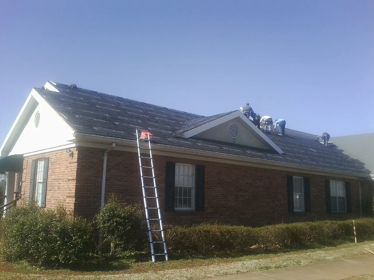 Crew tearing shingles off a brick ranch roof with a ladder set — Emergency Roof Repair work by our crew in Enola