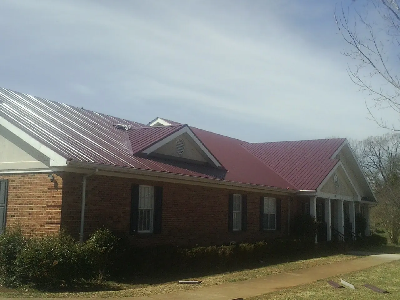 Red metal roof with gabled entries on a long brick building, from a Hail Damage Roof Repair job in Enola