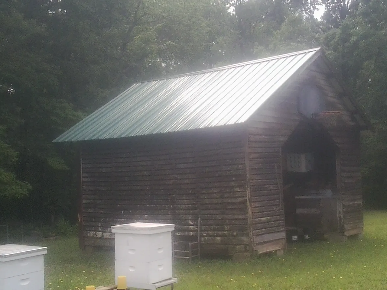 Green metal roof on a weathered barn beside stacked beehives in Enola
