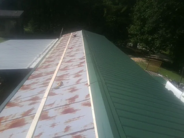 Old rusted panels beside newly installed green metal roofing — Wind Damage Roof Repair by Roofing Brothers in Enola