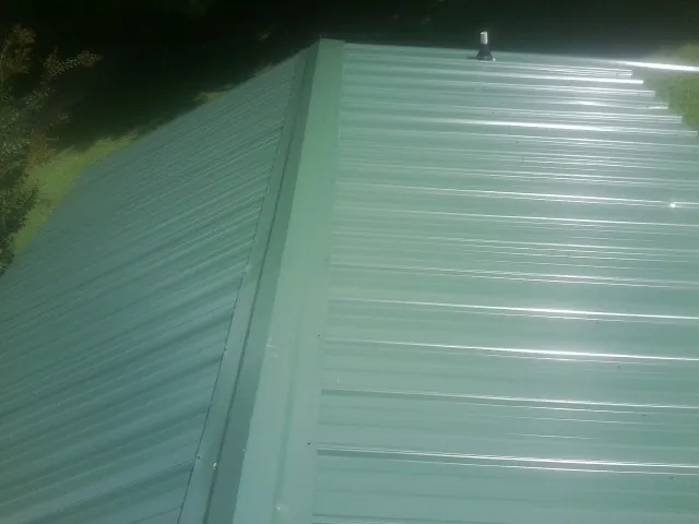New green metal panels meeting at the ridge of a roof — Flat Roof Repair work by our crew in Enola