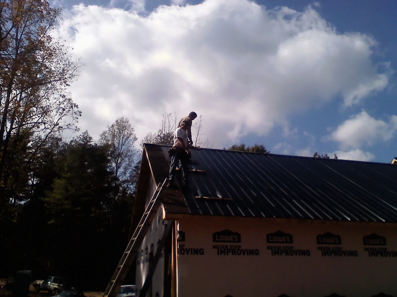 Roofer fastening dark metal panels high against a cloudy sky, from a Roof Inspection job in Enola