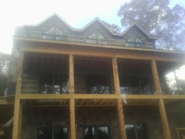 Dormers and porch framing on a large log home under construction — Roof Coating work by our crew in Enola