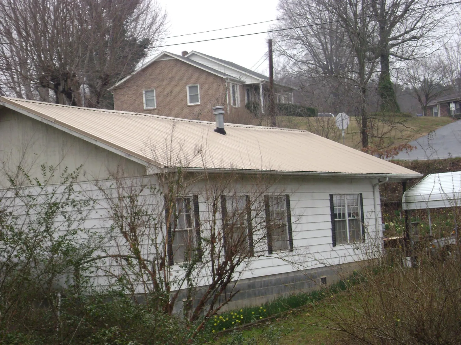 Tan metal roof on a white sided house set into a hillside — Commercial Roofing by Roofing Brothers in Enola