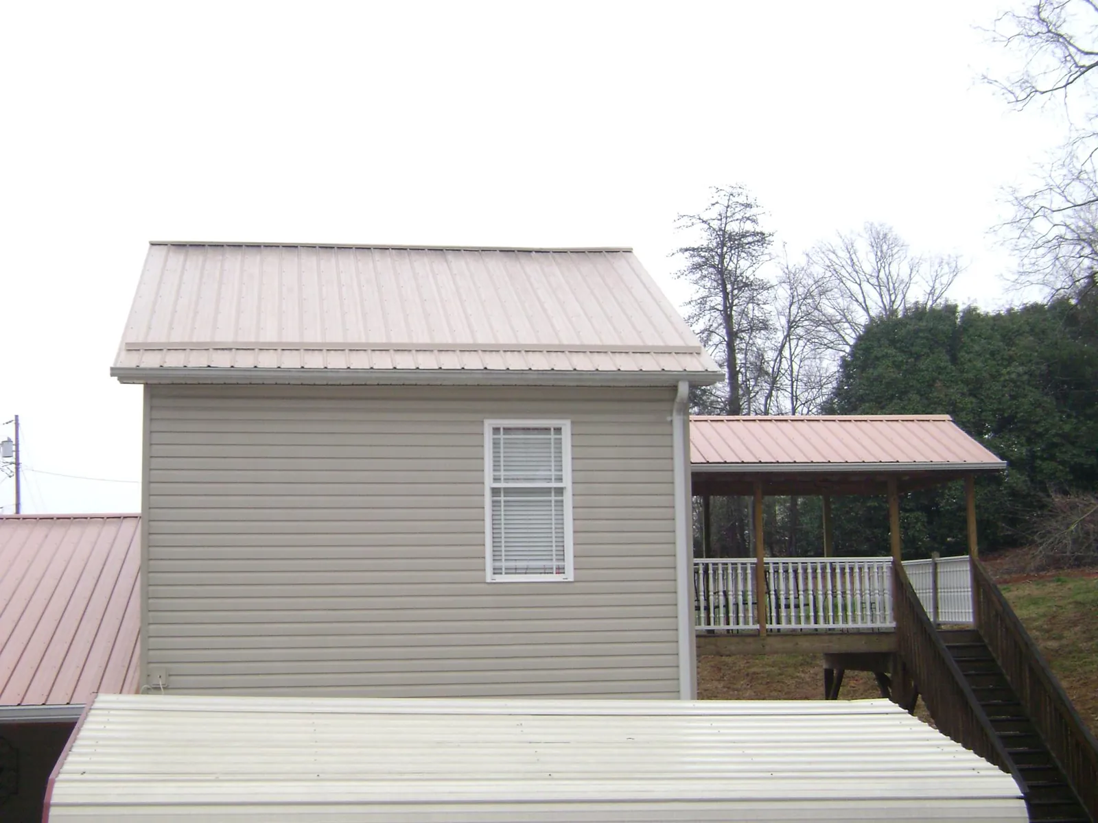 Tan metal roofs on a two story addition and attached porch, from a Roof Replacement job in Enola